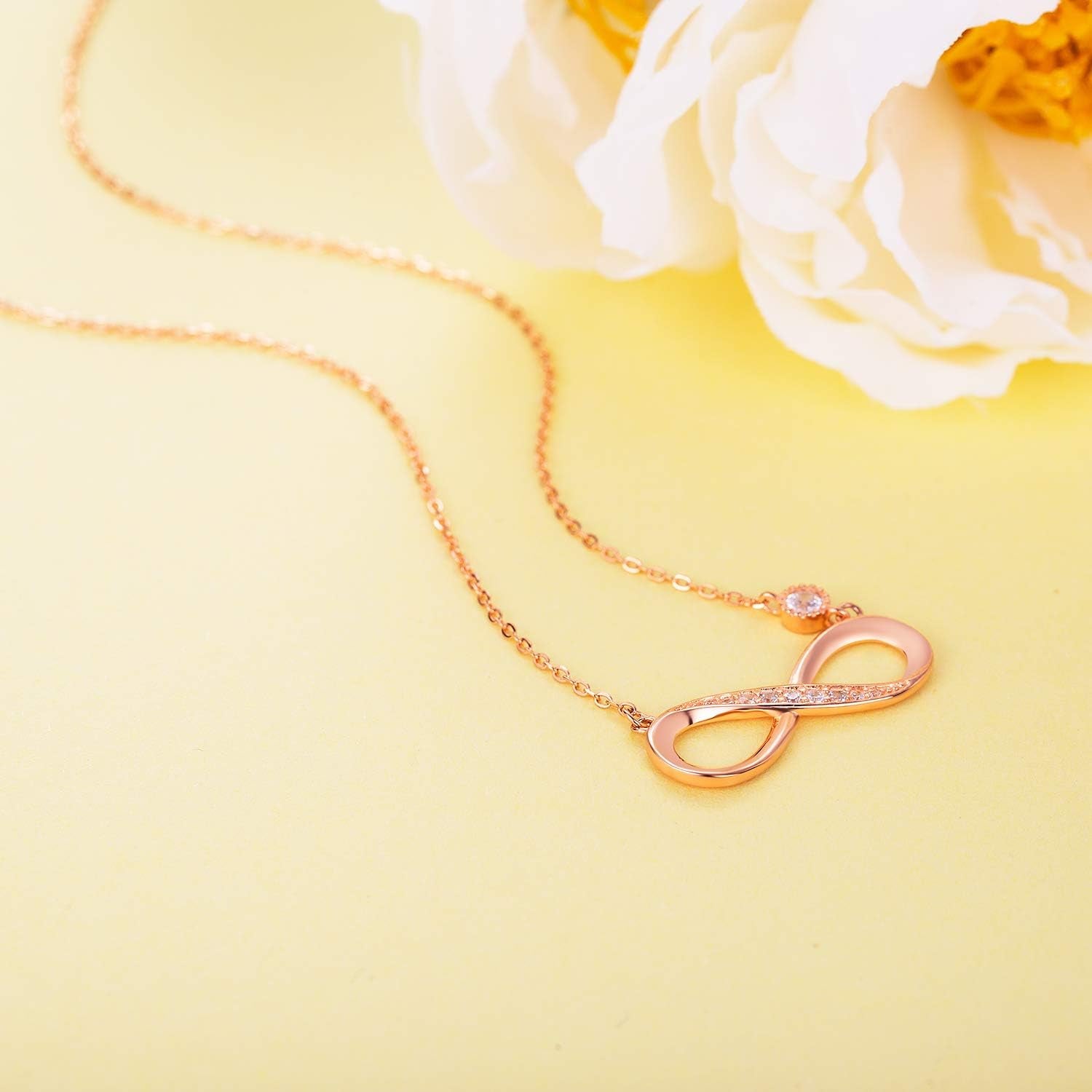 Infinity Necklace 925 Sterling Silver with rose gold infinity pendant and sparkling detail, on a soft yellow background.
