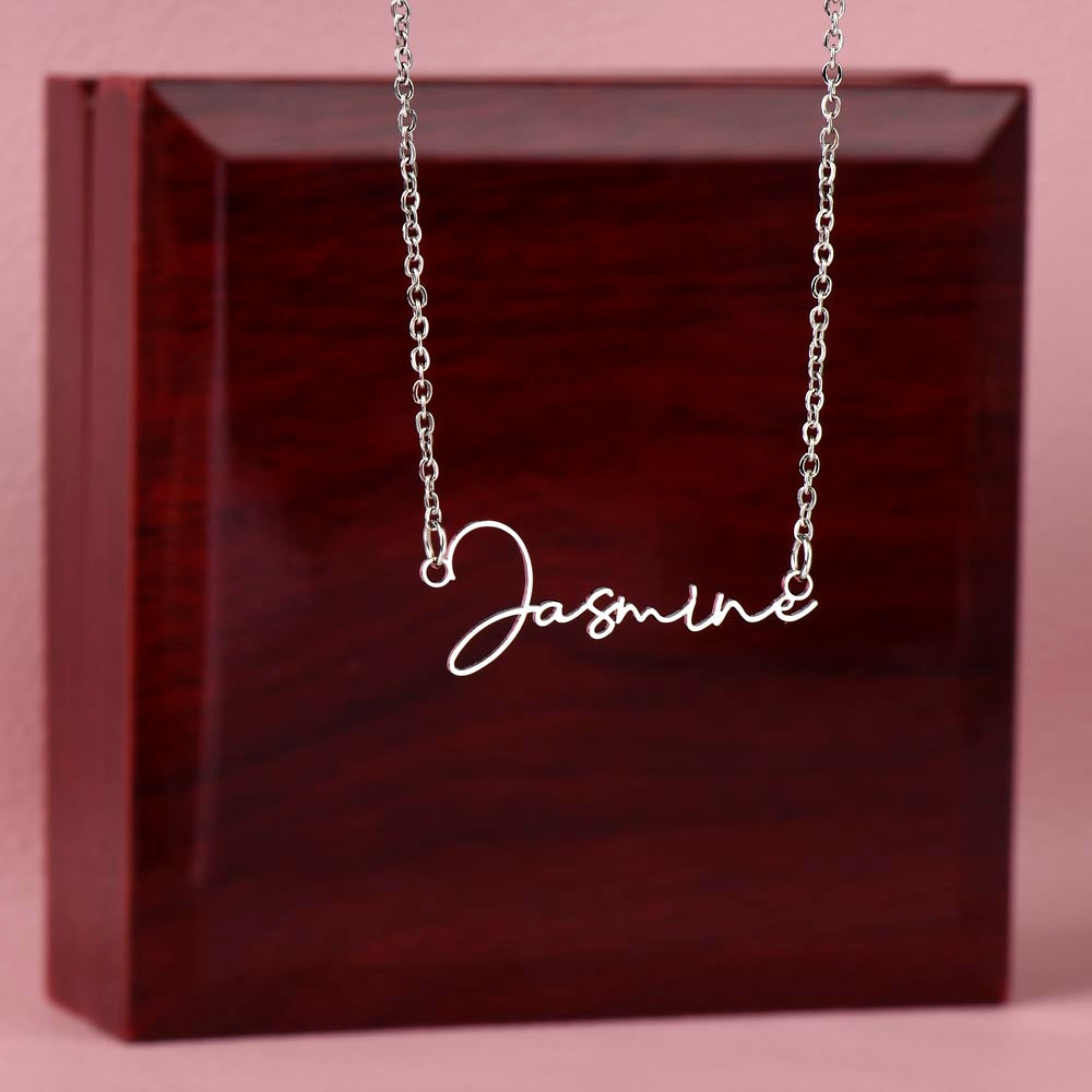 Personalized name necklace with the name Jasmine displayed, hanging in front of a wooden jewelry box.